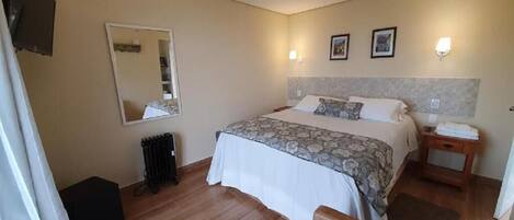 A bedroom with a bed, bedside table, lamp, mirror, and a radiator.