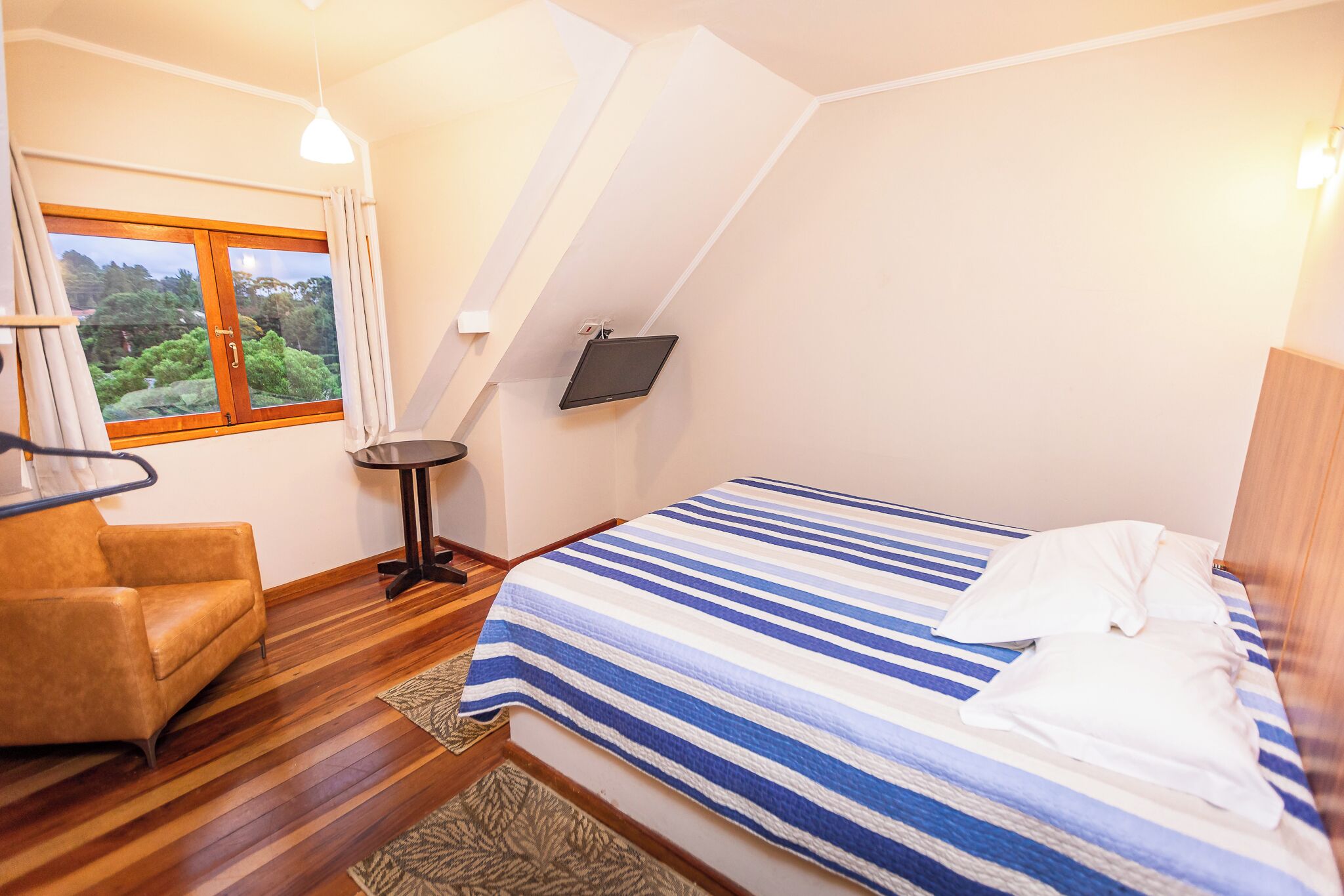 A bedroom with a bed, a chair, a small table, and a TV.