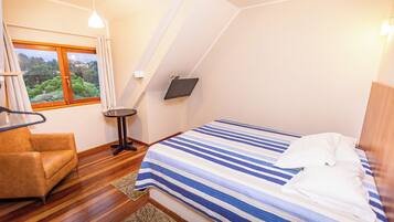 Um quarto com uma cama, uma cadeira, uma mesinha e uma televisão.