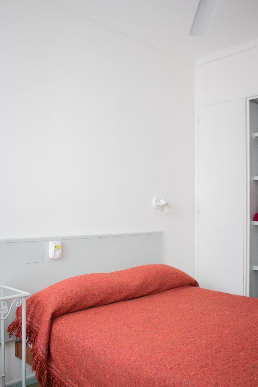 A room with a bed, a white wardrobe, and a white wall.