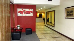 Vestíbulo de hotel con pared roja, un cuadro de flores rojas, mostrador de recepción y un espejo grande.