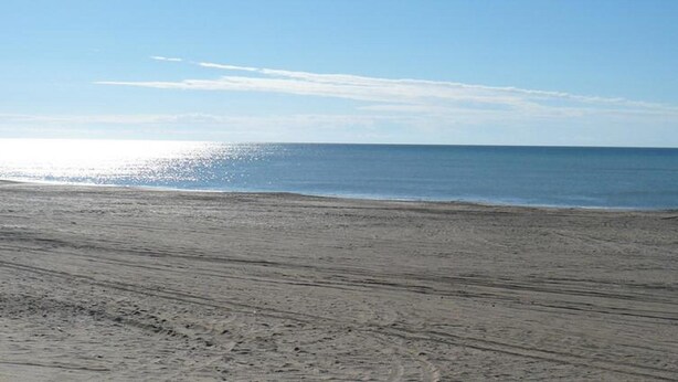 Ein weiter Sandstrand mit sanften Wellen und blauem Himmel.