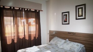 Ein Hotelzimmer mit einem Bett, Vorhängen und zwei gerahmten Bildern an der Wand.