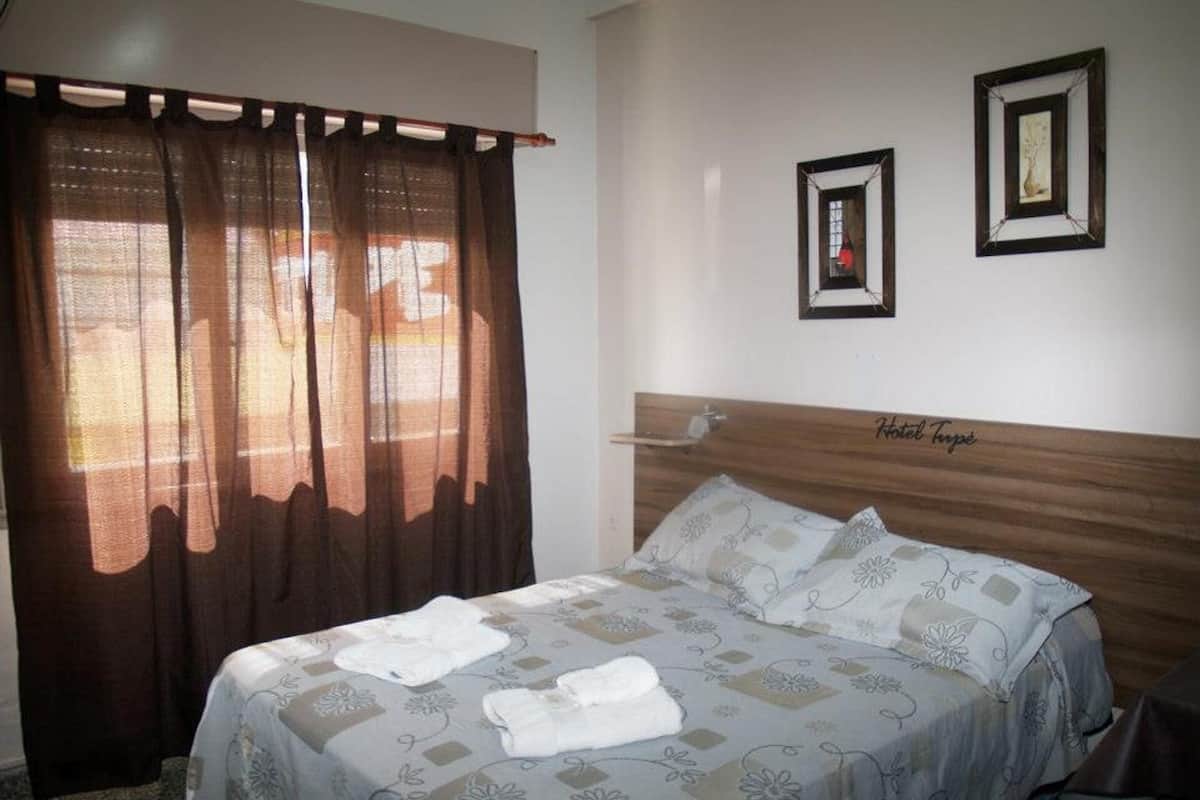 Ein Hotelzimmer mit einem Bett, Vorhängen und zwei gerahmten Bildern an der Wand.