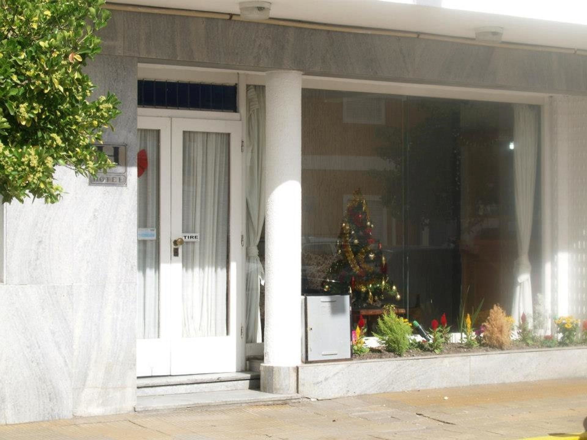 Una entrada de hotel con un ventanal grande, una puerta con un letrero que dice 'TIRE' y un árbol de Navidad en la ventana.