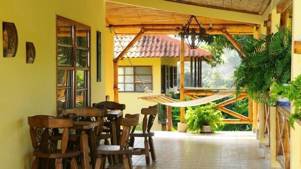 A covered outdoor area with a wooden table and chairs, a hammock, and potted plants. - La Granja Campo Y Aventura (Cativa)