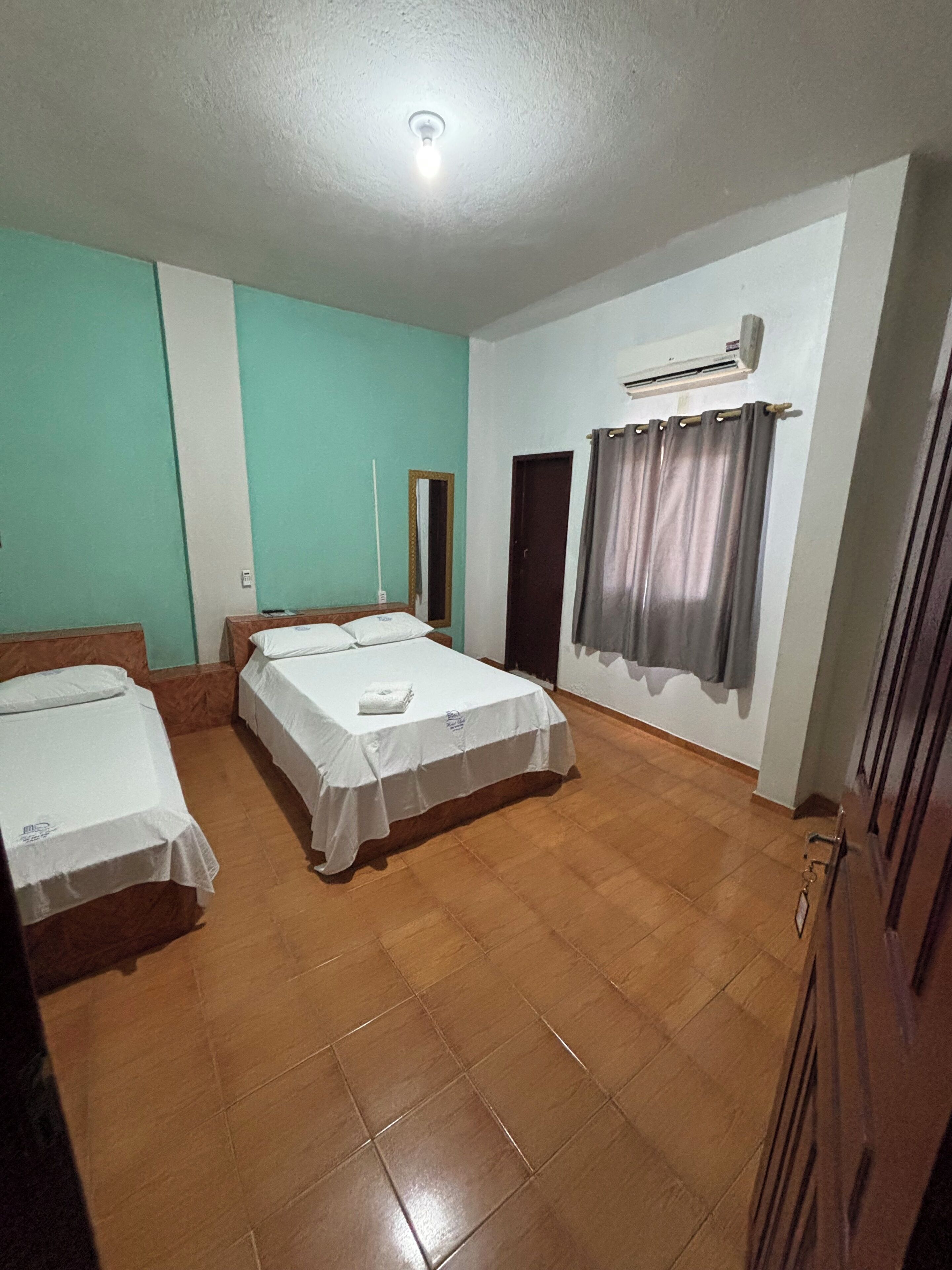 Une chambre avec deux lits, un luminaire au plafond, un appareil de climatisation, une porte et un rideau.