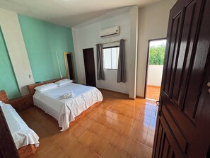 Ein Hotelzimmer mit Bett, Nachttisch, Spiegel, Klimaanlage und Blick auf Grün.