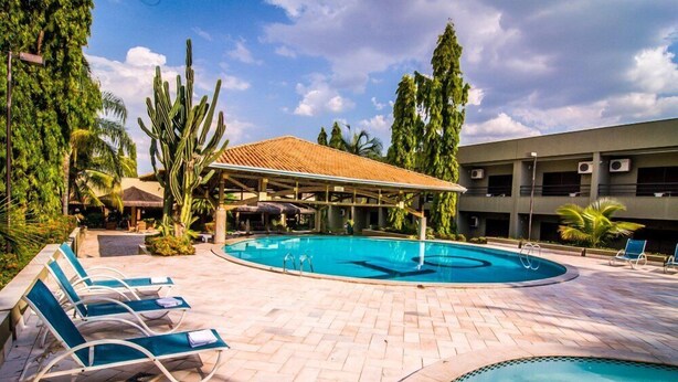 A swimming pool with lounge chairs, surrounded by palm trees and a building with air conditioning units. - Hotel OT (Tres Lagoas)