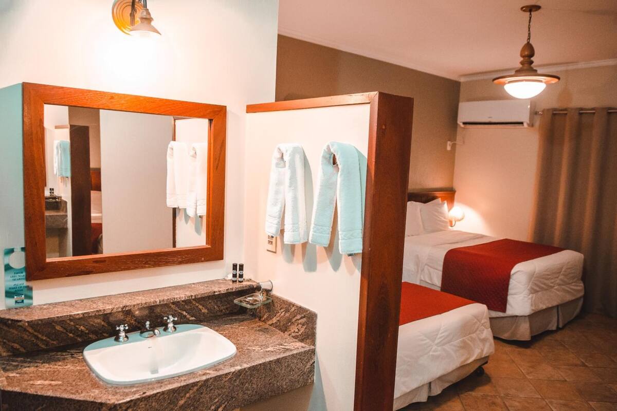 A hotel room with a marble sink, a large mirror, two beds with red and white bedding, and a ceiling fan.