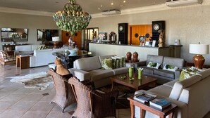 A spacious living room with a large chandelier, comfortable seating, and a reception area with a counter and clocks. - Hotel OT (Tres Lagoas)