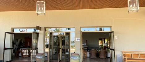 A hotel entrance with a wooden ceiling, glass doors, and a bench outside.