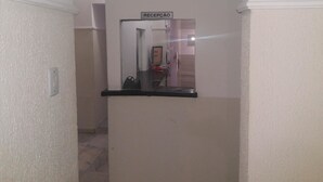 Un corridoio con la segnaletica della reception, una porta e uno specchio che riflette una stanza con un letto e una finestra.