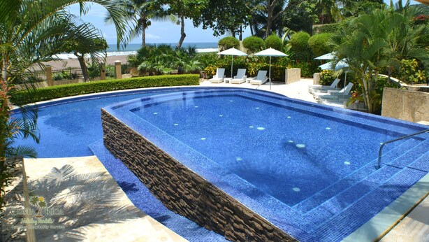 Une piscine bordée de pierres, entourée de chaises longues et de parasols, avec vue sur l’océan.