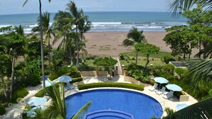 Une piscine avec vue sur la plage et l’océan, entourée de palmiers et de chaises longues.