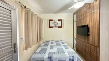 A bedroom with a bed, a ceiling fan, a TV mounted on the wall, and a door with a curtain.