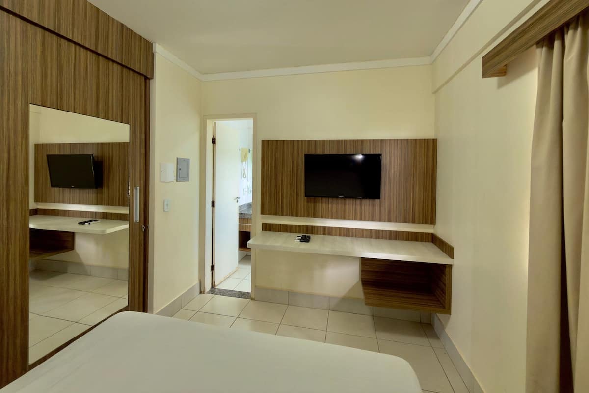 Une chambre d’hôtel comprenant un lit, un téléviseur fixé sur un panneau en bois, un miroir et une porte donnant sur une salle de bain.