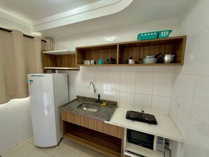 Eine kompakte Küche mit Kühlschrank, Spüle, Mikrowelle und Holzregalen über der Arbeitsplatte.