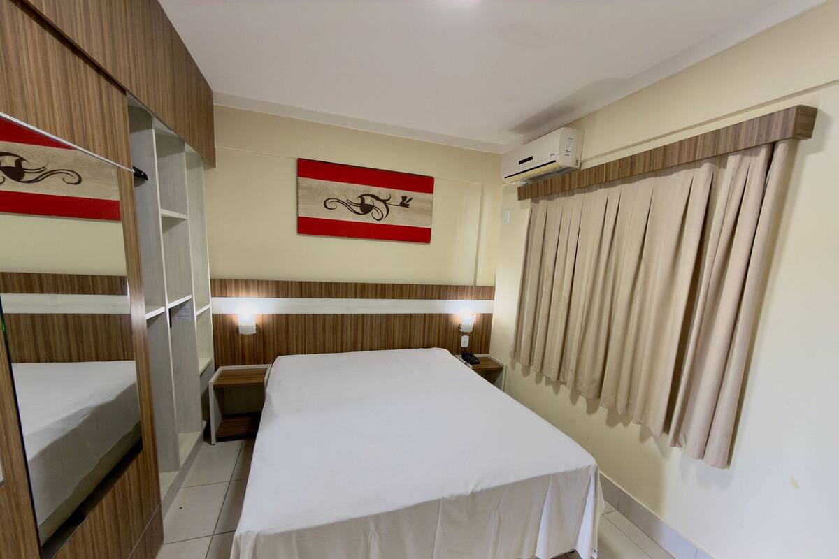 Une chambre d’hôtel équipée d’un lit, de tables de chevet, d’un appareil de climatisation et de rideaux.