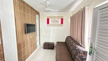 A hallway with a ceiling fan, a flat-screen TV mounted on a wooden panel wall, a bench with floral upholstery, and a door with a window.