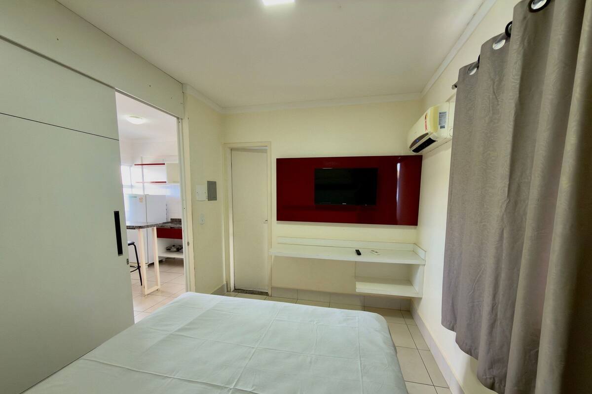 Une chambre d’hôtel avec un lit, un téléviseur fixé au mur, une armoire et une salle de bain visible à travers une porte ouverte.