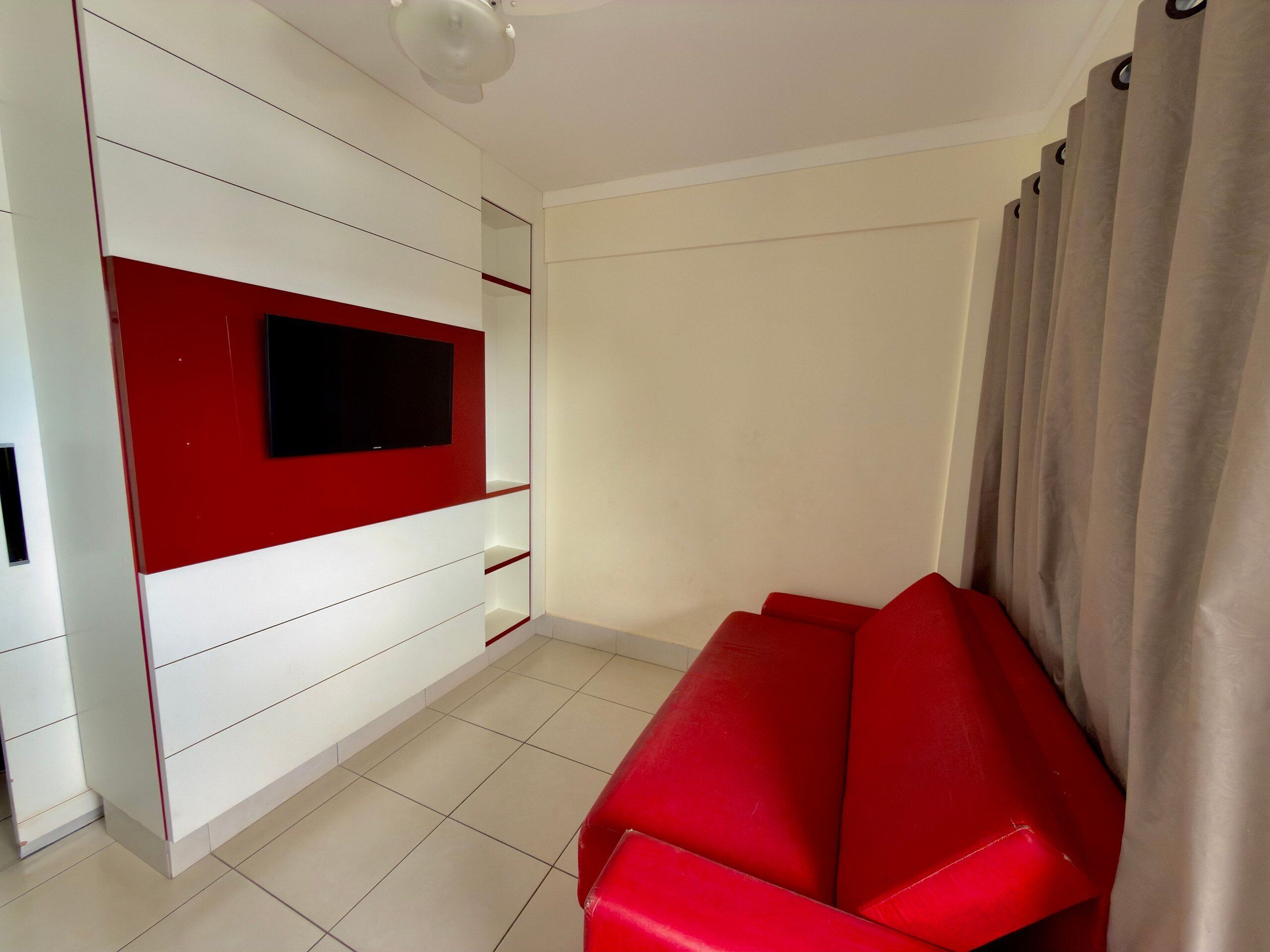 Una sala moderna con un sofá rojo, un mueble empotrado blanco para entretenimiento y un ventanal con cortinas.