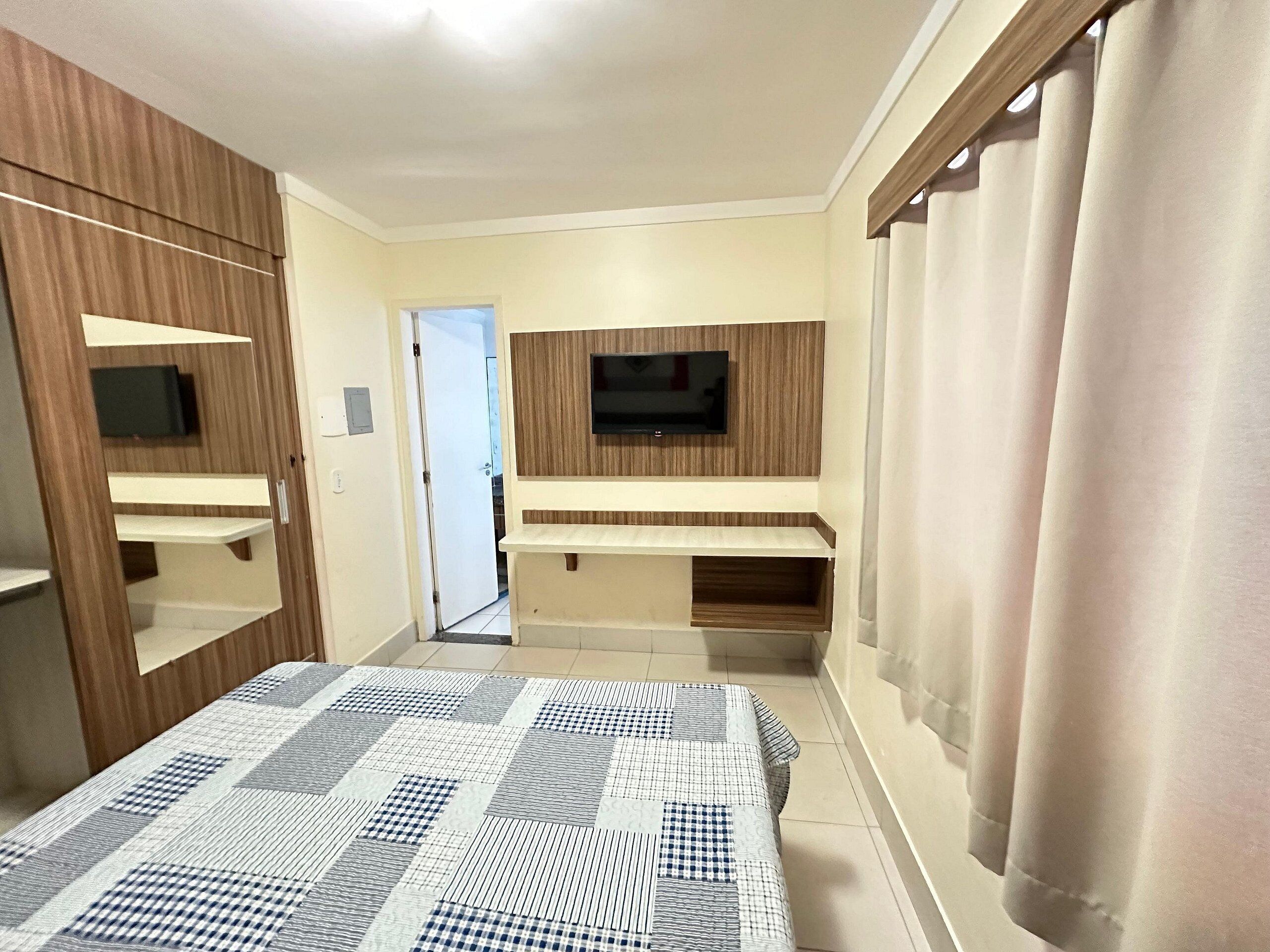 A bedroom with a bed, a TV mounted on the wall, and a wardrobe.