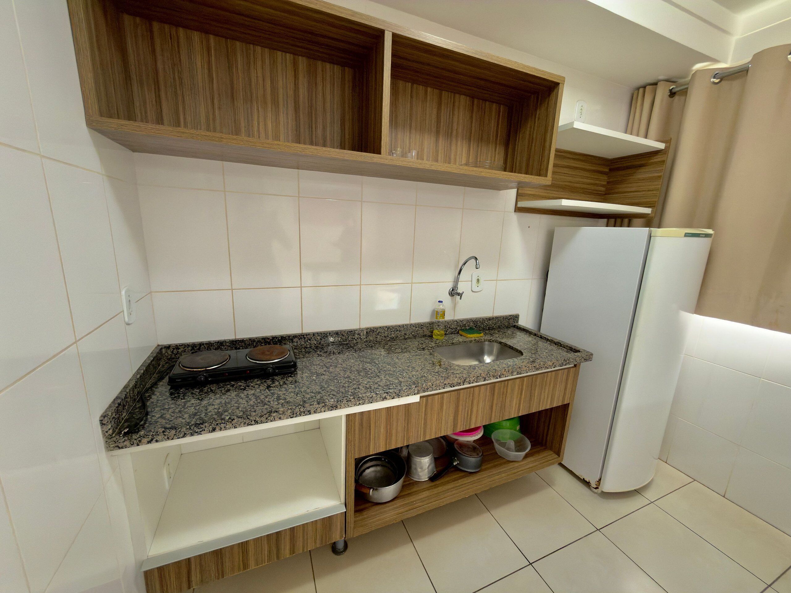 Una cocina compacta con encimera de granito, pileta de acero inoxidable, armarios de madera y un refrigerador blanco.
