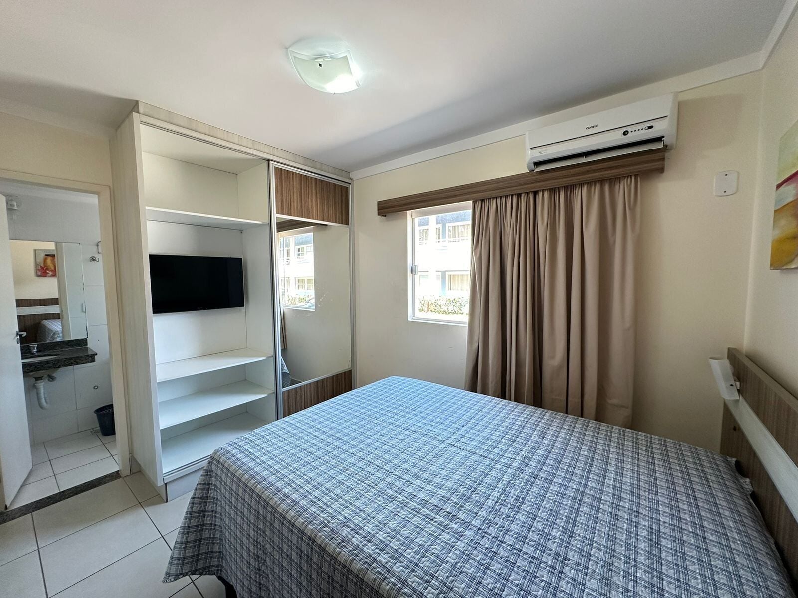 A bedroom with a bed, a TV, a wardrobe, and an air conditioning unit.