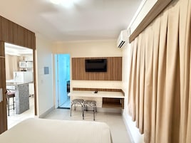 Quarto de hotel com uma cama, uma escrivaninha com duas cadeiras, uma televisão e um aparelho de ar condicionado.