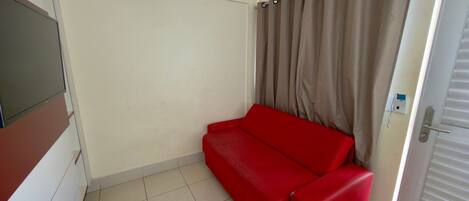 A room with a red sofa, a door with a window, and a wall-mounted electrical outlet.