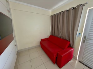 A room with a red sofa, a door with a window, and a wall-mounted electrical outlet.