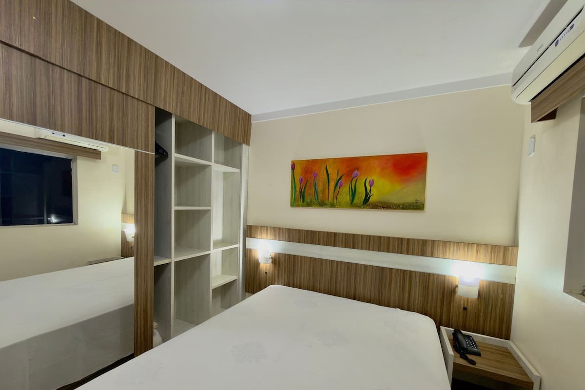 Une chambre d’hôtel avec un lit, un tableau, un bureau avec un téléphone et une armoire.