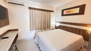 A hotel room with a bed, a desk with a chair, a flat-screen TV, an air conditioner, and a window with curtains. - Lacqua Di Roma I Via Caldas (Caldas Novas)