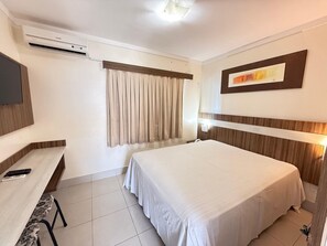 A hotel room with a bed, a desk with a chair, a flat-screen TV, an air conditioner, and a window with curtains. - Lacqua Di Roma I Via Caldas (Caldas Novas)