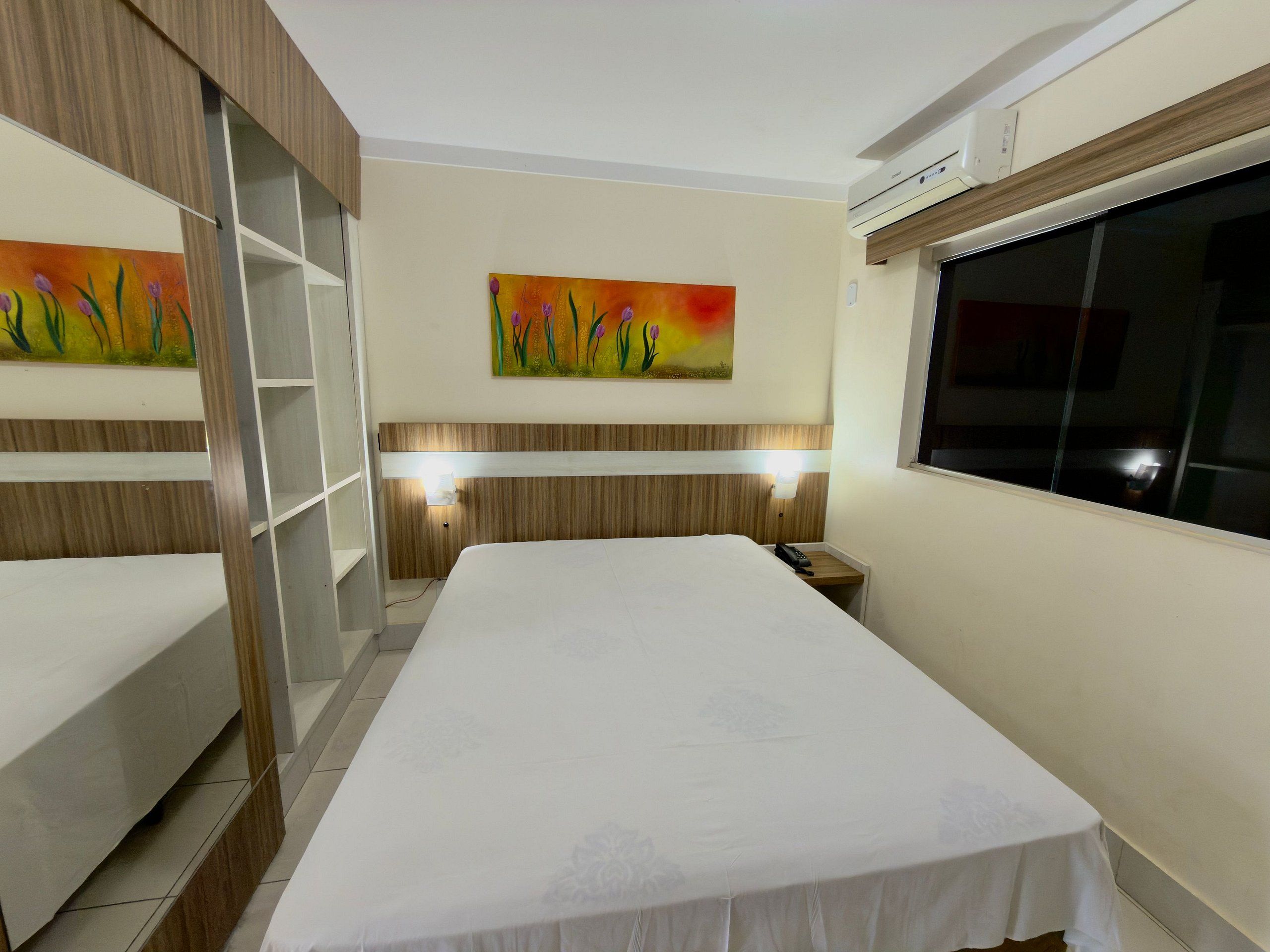 Una habitación de hotel con una cama, una mesita de noche, una ventana y un cuadro en la pared.