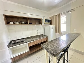 Una cocina con gabinetes blancos, encimera de granito, microondas y refrigerador.