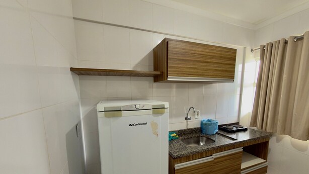 A compact kitchen with white cabinets, a countertop, a sink, and a built-in refrigerator. - Lacqua Di Roma I Via Caldas (Caldas Novas)