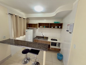 A compact kitchen with a refrigerator, sink, microwave, and a small bar stool.