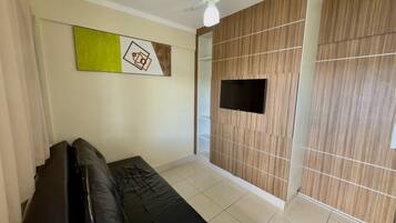 A living room with a black sofa, a flat-screen TV mounted on a wooden panel wall, a ceiling fan, and a large abstract painting.