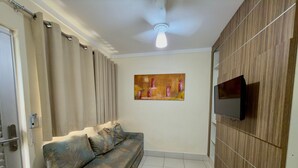 A living room with a sofa, a flat-screen TV, a ceiling fan, and a painting on the wall. - Lacqua Di Roma I Via Caldas (Caldas Novas)