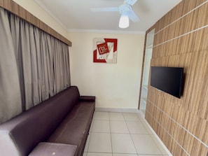 A room with a sofa, a ceiling fan, a mounted TV, and a wall with a patterned design. - Lacqua Di Roma I Via Caldas (Caldas Novas)