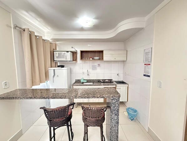 A compact kitchen with a microwave, stove, and two wicker chairs. - Lacqua Di Roma I Via Caldas (Caldas Novas)