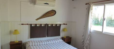 A bedroom with a bed, two bedside tables, a wall-mounted air conditioner, a decorative feather, and a window with curtains.