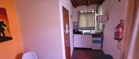 A narrow hallway with a kitchen area, a white refrigerator, a fire extinguisher, and a door with a notice.
