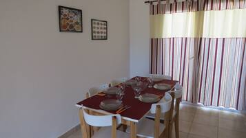 Comedor con mesa dispuesta para seis, sillas blancas y una cortina a rayas al fondo.
