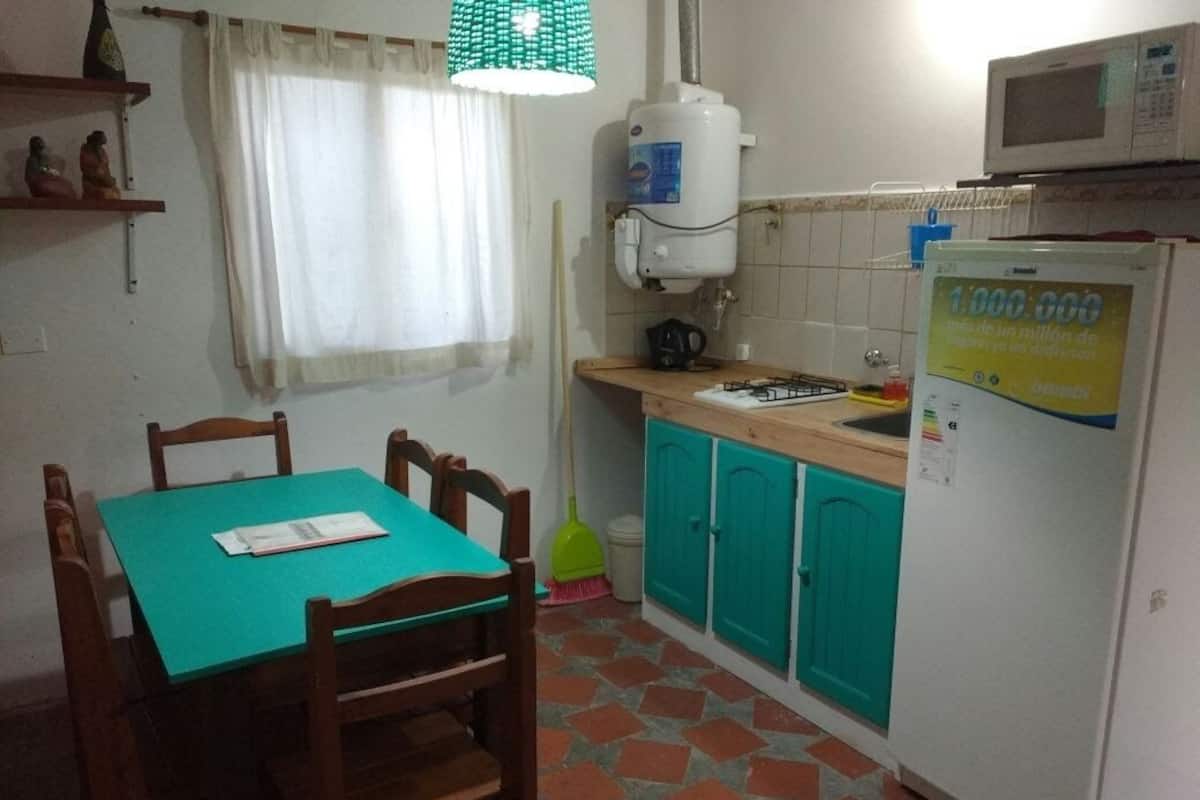 Cocina compacta con una mesa, sillas, refrigerador, microondas y calentador de agua.