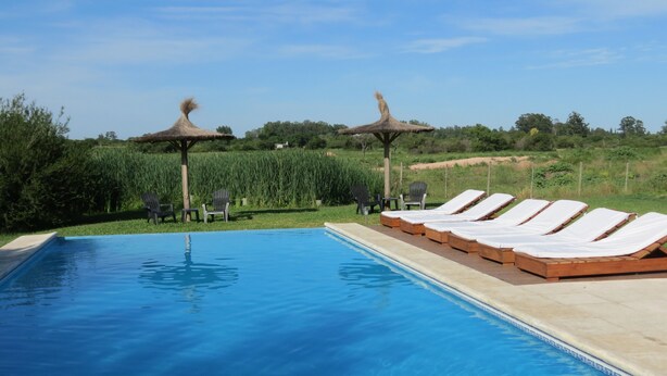 Una piscina con sillas de descanso y dos estructuras de techo de paja.