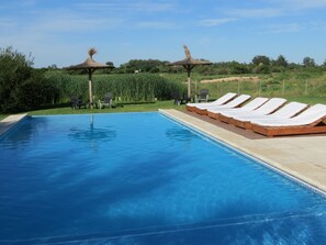 Una piscina con sillas de descanso y dos estructuras de techo de paja.