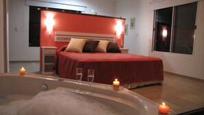 Un dormitorio con una cama grande, una mesita de noche, una ventana y una bañera con velas.